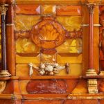 Fragment ściany korpusu szkatuły w odcieniach mlecznego , żółtego i miodowego bursztynu. Widoczne motywy zdobnicze w formie ornamentu roślinnego.
